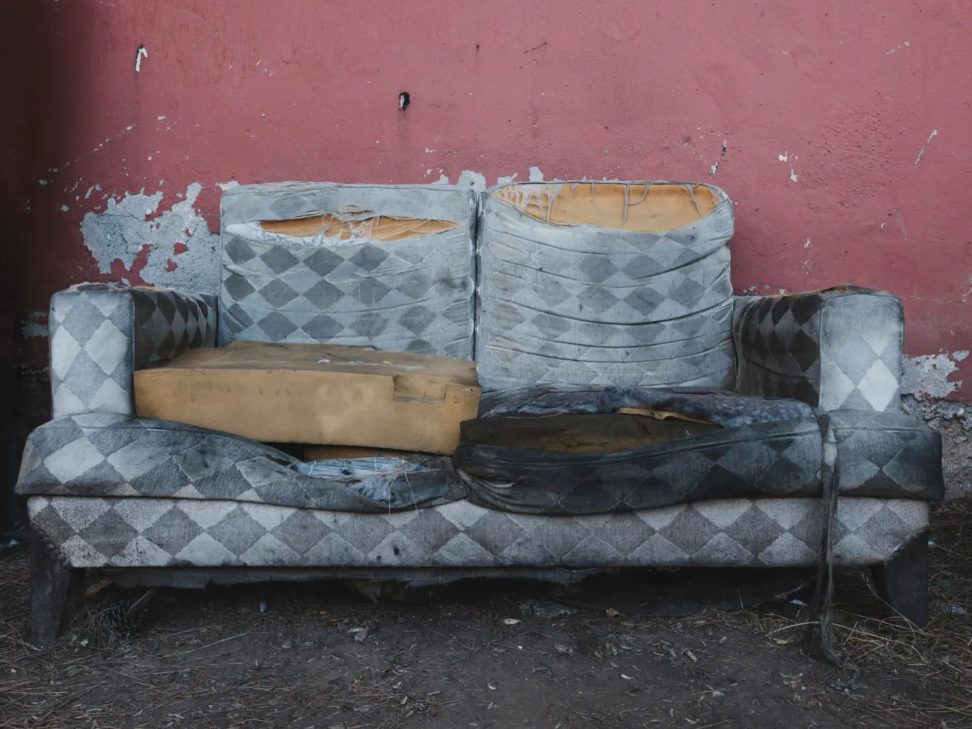 Sena nudėvėta sofa su suplyšusiu apmušalu lauke prie sienos