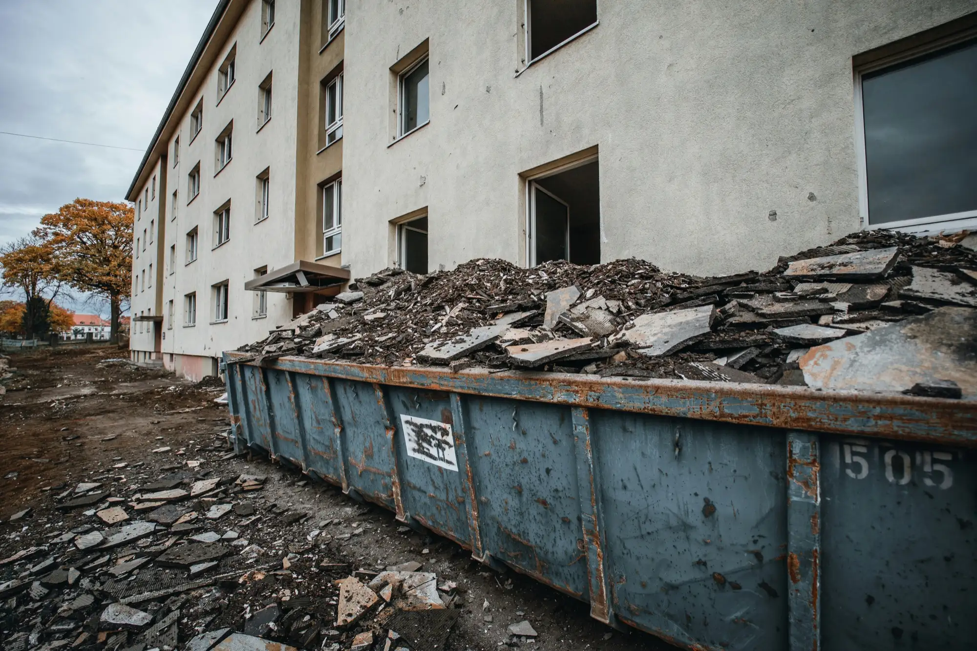 Metalinis konteineris, pilnas statybinių atliekų, prie daugiabučio namo kieme